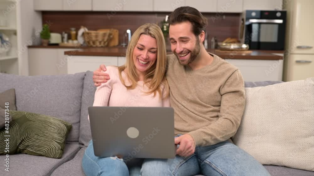 Serene couple spending time together at home, using laptop for spend leisure. Young wife pointing at the screen while resting on the sofa in modern apartment with her husband, watching movie together Serene couple spending time together at home, using laptop for spend leisure. Young wife pointing at the screen while resting on the sofa in modern apartment with her husband, watching movie together