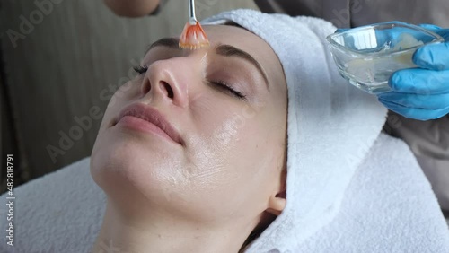 A young beautiful girl lies on the table at the beautician, hands in blue gloves apply a moisturizing cream, a mask with a brush   