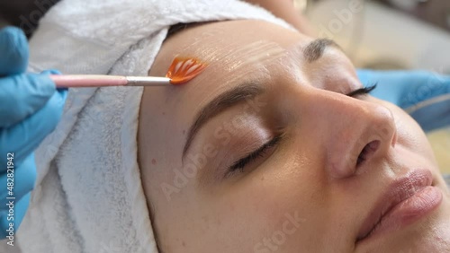 A young beautiful girl lies on the table at the beautician, hands in blue gloves apply a moisturizing cream, a mask with a brush   