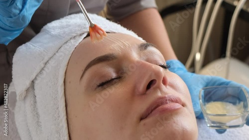 A young beautiful girl lies on the table at the beautician, hands in blue gloves apply a moisturizing cream, a mask with a brush   