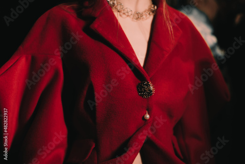 Part of a female body dressed in an elegant red jacket with golden buttons. Women's fashion and accessories