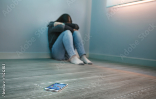 Unrecognizable woman covering her face desperate for cyberbullying with mobile on the floor photo