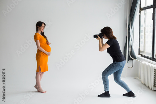 pregnant woman at a photo shoot in the studio, process of photoshooting. Photographer with model