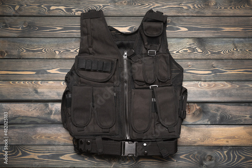 Black unloading vest on the wooden table flat lay background.