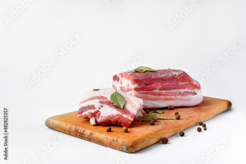 bacon sliced on a wooden board with spices on a white background