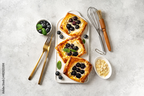 Mini puff pie with cheese cream, almonds, and blueberries in a plate on the kitchen table. Delicious layered square with berries, dorblue or ricotta, nuts on a culinary background. Top view photo