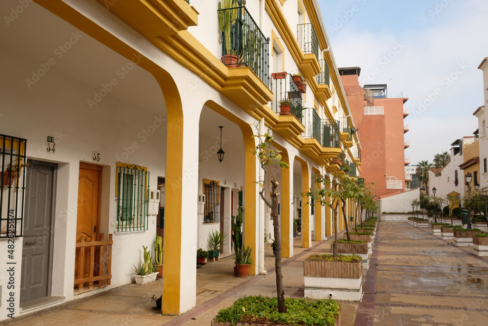 Obraz premium View of residential building with an arch. Apartments with windows, balconies and entrance, typical spanish architecture. Alley with green plants in pots on street. Torremolinos, Andalusia, Spain.