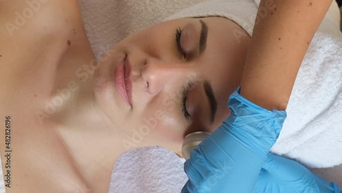 Young woman lying on cosmetologist's table during rejuvenation procedure. Cosmetologist take care about neck and face skin youthfull and wellness. Hardware face cleaning procedure  