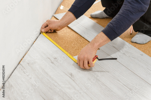 Unrecognizable man laying laminate flooring. Professional laying of flooring - laminate. Measuring tape on laminate floor plank
