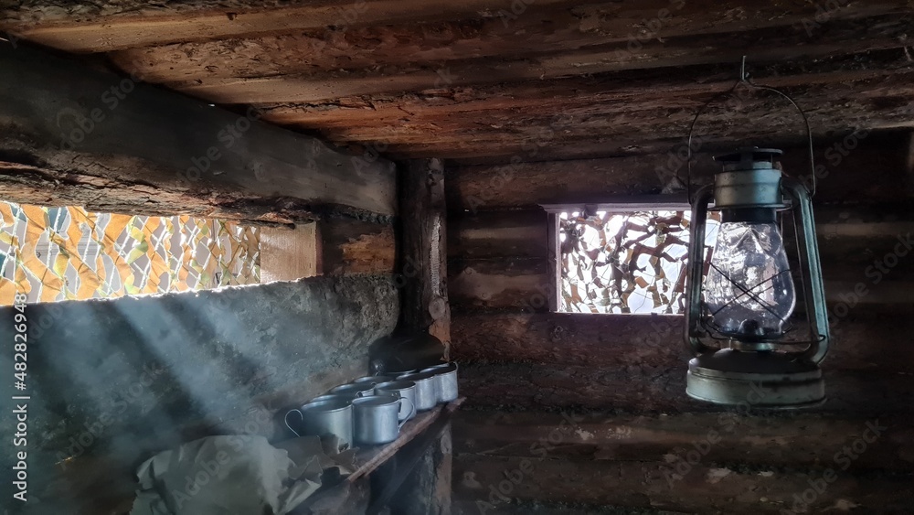 A wooden dugout in which a kerosene lamp burns. Light from the window penetrates into the room. A wooden dugout in which a kerosene lamp burns. Light from the window penetrates into the room.