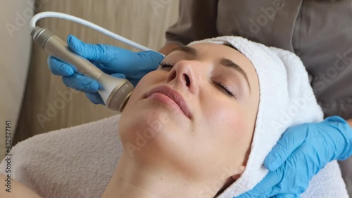 Young woman lying on cosmetologist's table during rejuvenation procedure. Cosmetologist take care about neck and face skin youthfull and wellness. Hardware face cleaning procedure  