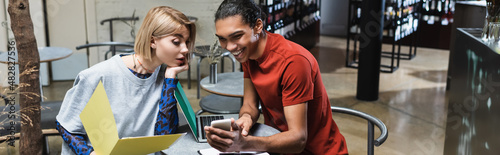 Positive interracial freelancers using smartphone in cafe, banner.