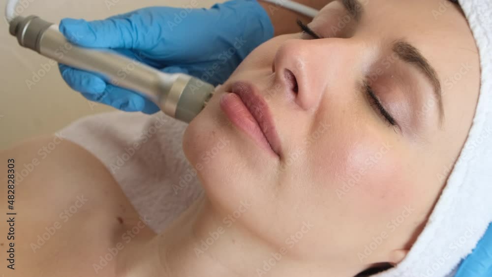 Young woman lying on cosmetologist's table during rejuvenation procedure. Cosmetologist take care about neck and face skin youthfull and wellness. Hardware face cleaning procedure Young woman lying on cosmetologist's table during rejuvenation procedure. Cosmetologist take care about neck and face skin youthfull and wellness. Hardware face cleaning procedure