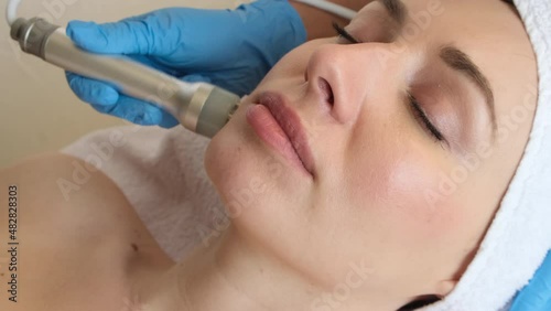 Young woman lying on cosmetologist's table during rejuvenation procedure. Cosmetologist take care about neck and face skin youthfull and wellness. Hardware face cleaning procedure  