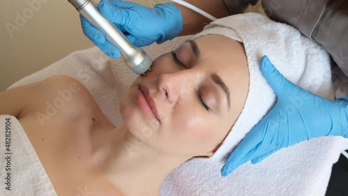 Young woman lying on cosmetologist's table during rejuvenation procedure. Cosmetologist take care about neck and face skin youthfull and wellness. Hardware face cleaning procedure  