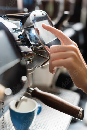 Cropped view of barista using coffee machine near cup in cafe.