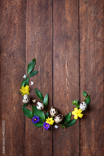 Flat lay composition with natural Easter eggs,fresh flowers egg shaped, blank card on wooden background, space for text.