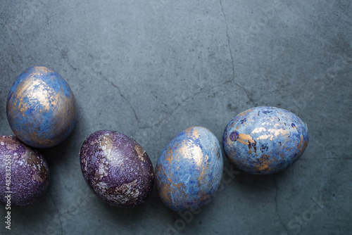 Easter card with a copy of the place for the text. Purple, blue and golden eggs on a dark background. The trend of 2022 purple shade is very peri. Natural dye karkade tea. Top view.
