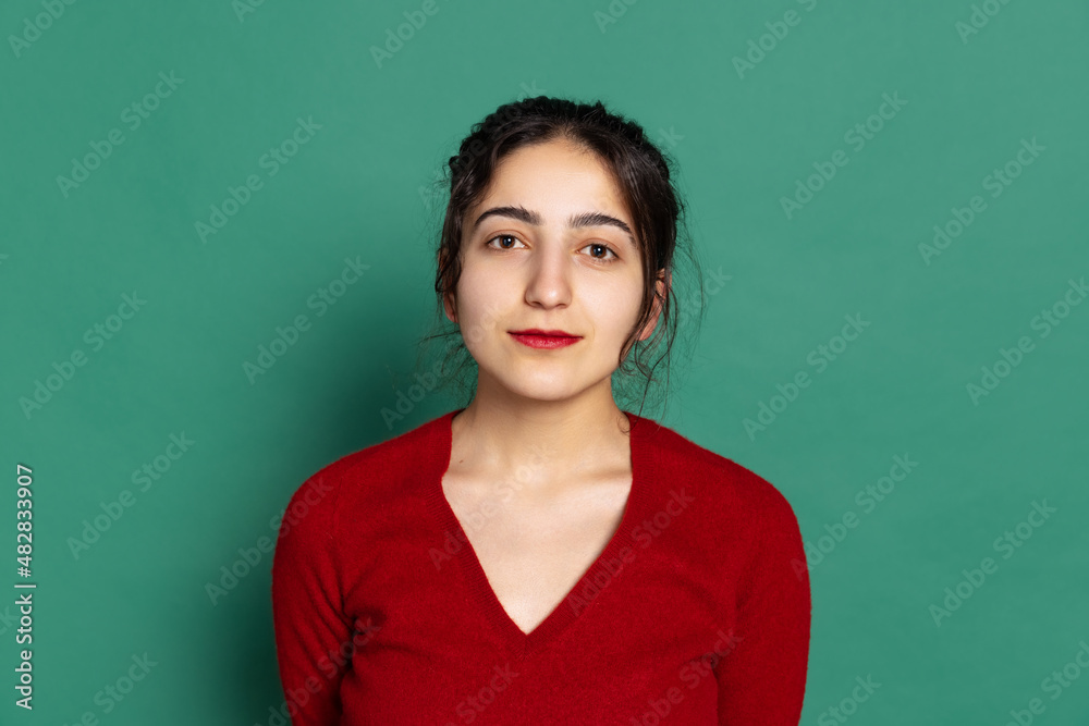 Studio shot of young pretty girl in red pullover looking at camera isolated on green background. Concept of emotions, facial expressions Studio shot of young pretty girl in red pullover looking at camera isolated on green background. Concept of emotions, facial expressions