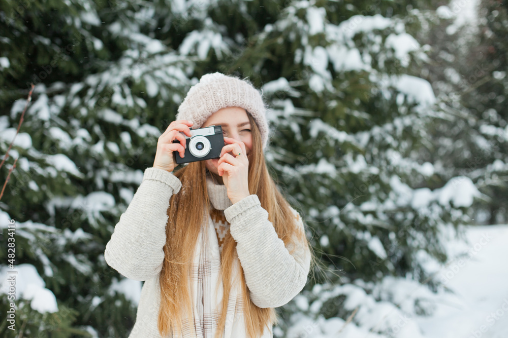 Beautiful millennial young woman taking pictures with retro vintage film camera. Hobby and leisure activity in winter forest outside. Amateur photographer taking photos with snow. Beautiful millennial young woman taking pictures with retro vintage film camera. Hobby and leisure activity in winter forest outside. Amateur photographer taking photos with snow.