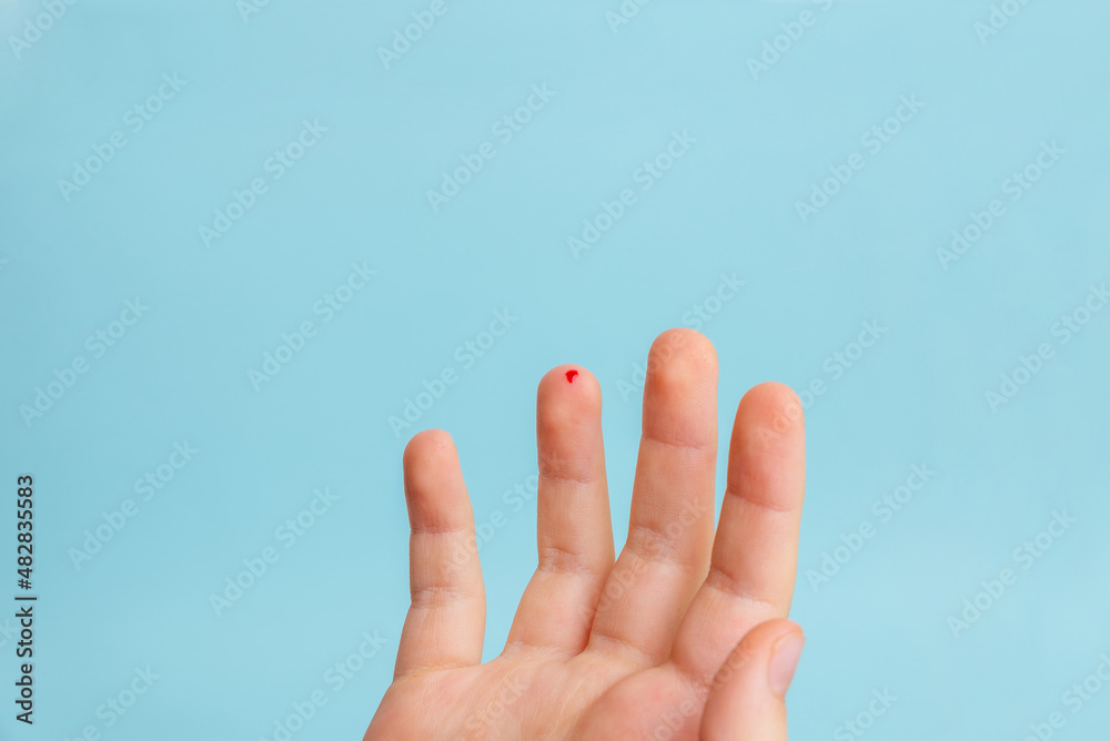 Drop of blood on a child's finger. The concept of measuring blood sugar levels with the help of strips. Blue background