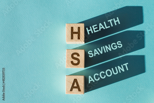 Wooden cubes with words HSA Health Savings Account with shadows. Beautiful blue background. Business and HSA concept.