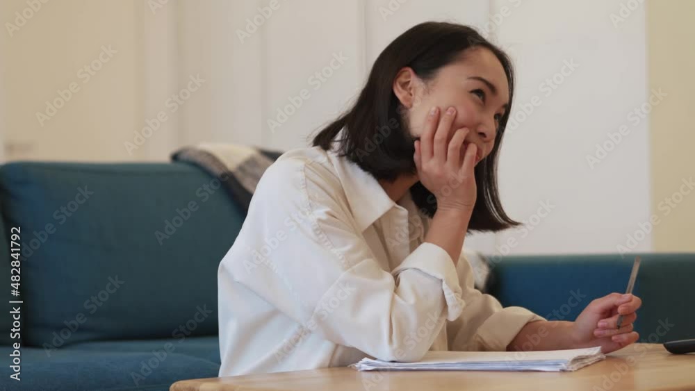 Pensive Asian woman writing something at home Pensive Asian woman writing something at home