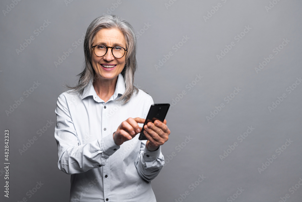 Happy business woman in formal shirt touching to the smartphone screen while feeling great with new phone features. Indoor studio shot isolated on grey background Happy business woman in formal shirt touching to the smartphone screen while feeling great with new phone features. Indoor studio shot isolated on grey background