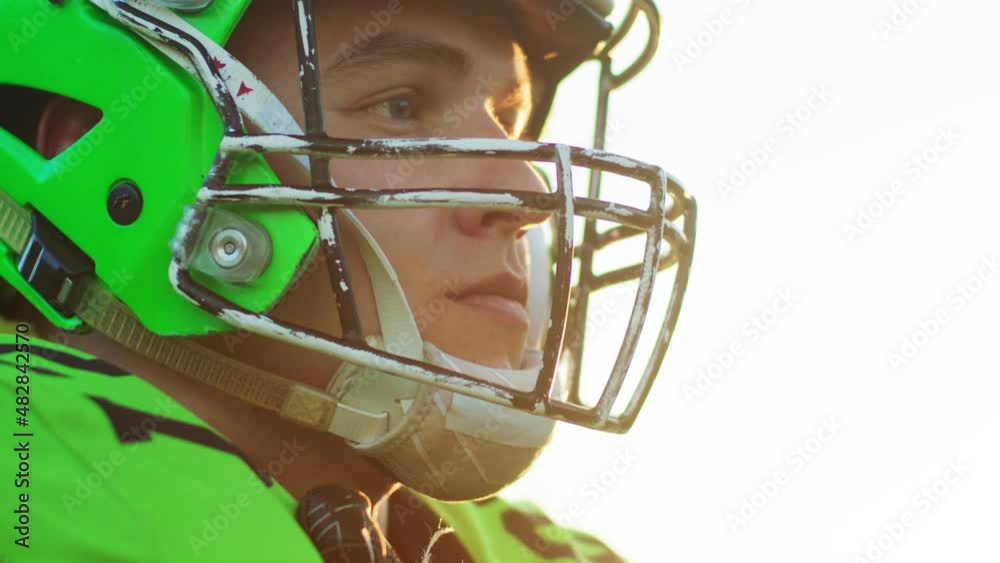 Side view of the male American football player standing in his protective helmet against bright stadium in the sun light. Sport concept
