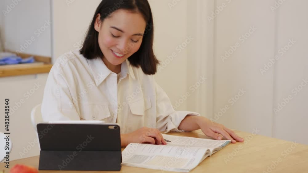 Smiling Asian woman studying distance learning on the tablet at home Smiling Asian woman studying distance learning on the tablet at home