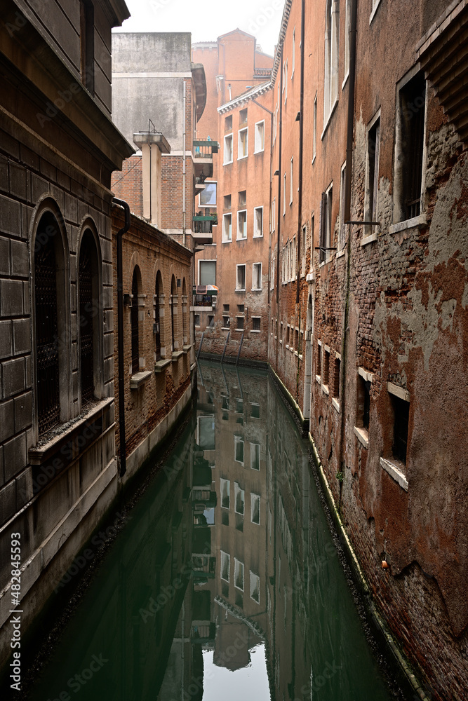 Die Roten Fassaden Venezianischer Häuser spiegeln sich im ruhigen Wasser eines Wasserkanal