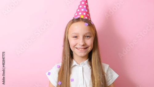 teenage girl in a festive cap throws up confetti on colored background close-up