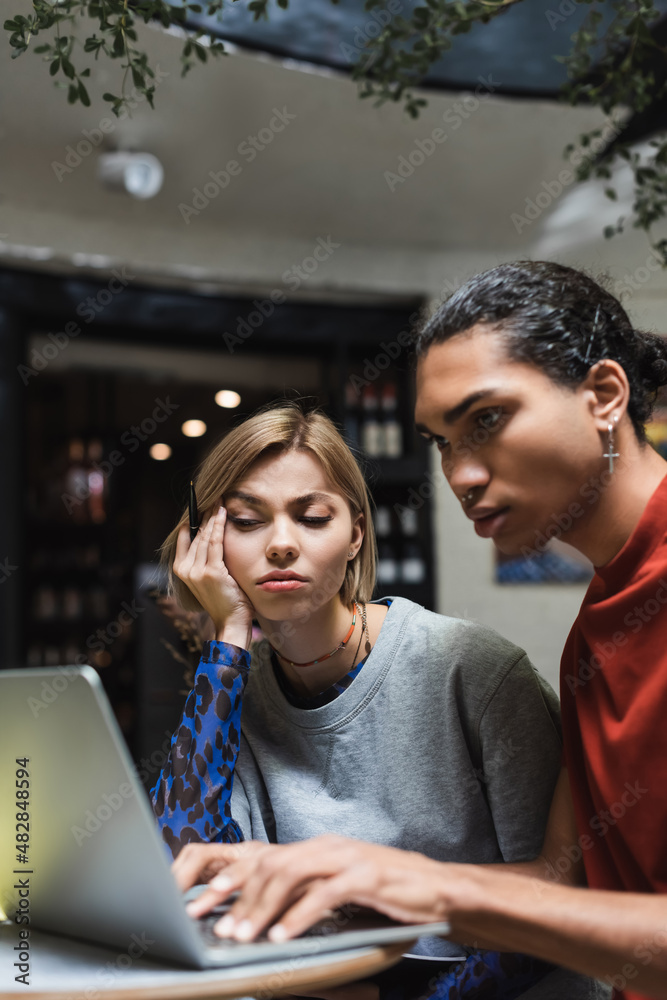 Upset freelancer looking at laptop near african american friend in cafe. Upset freelancer looking at laptop near african american friend in cafe.
