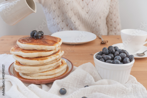 Breakfast pancakes scene with person about to pour sauce over the stack. Rustic light and airy feel with white light background and copy space available.