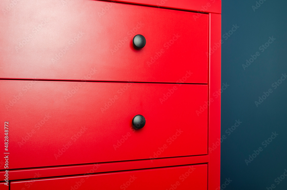 Red chest of drawers in a Scandinavian interior. A red wooden cabinet with black handles stands in an apartment