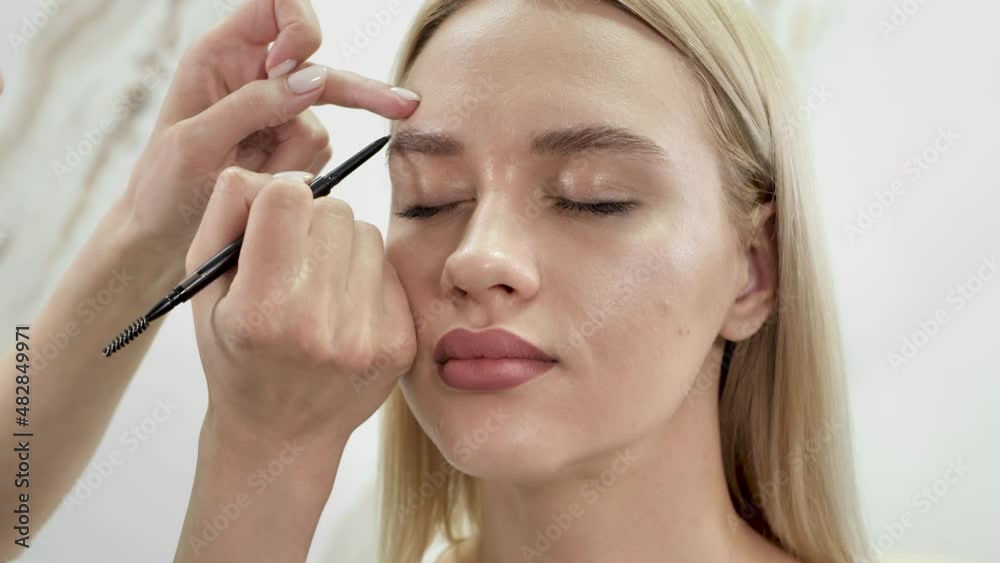 Stylist draws eyebrows with a pencil for a young beautiful woman Stylist draws eyebrows with a pencil for a young beautiful woman