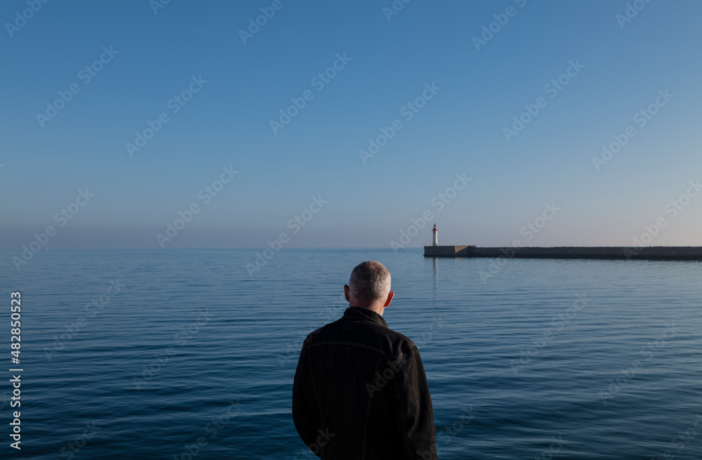 Naklejka premium Rear view of adult man against sea and sky with lighthouse in background. Almeria, Spain