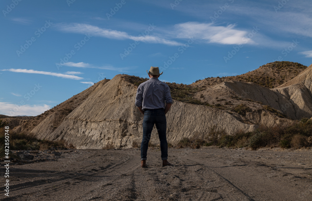 Rear view of adult man in cowboy hat standing against mountains in Tabernas desert. Almeria, Spain