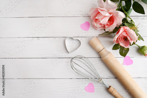 Valentine day baking background. Ingredients for cooking Valentine's hearts on white wood with pink flower roses. Top view copy space
