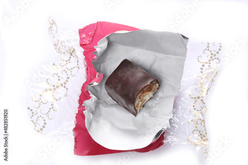 bitten chocolate candy  in a red open wrapper isolated on white background with copy space for your text.