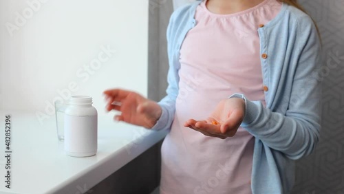 Teenage girl takes omega 3 capsules in the interior of the room