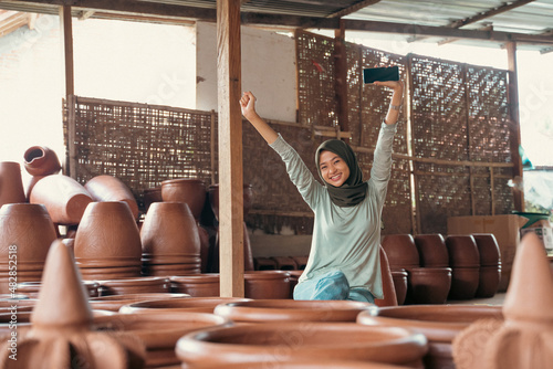 Muslim girl in hijab excited between pottery while using smartphone