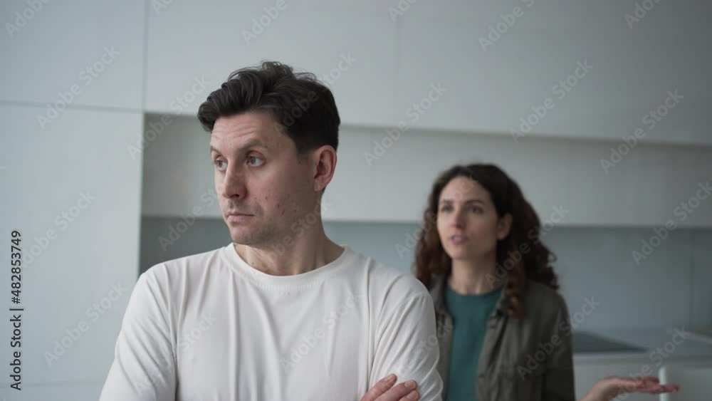 Family conflict. A sad husband looks thoughtfully out the window against the backdrop of a cursing and hysterical wife, spreads his arms and pushes him. Family conflict. A sad husband looks thoughtfully out the window against the backdrop of a cursing and hysterical wife, spreads his arms and pushes him.