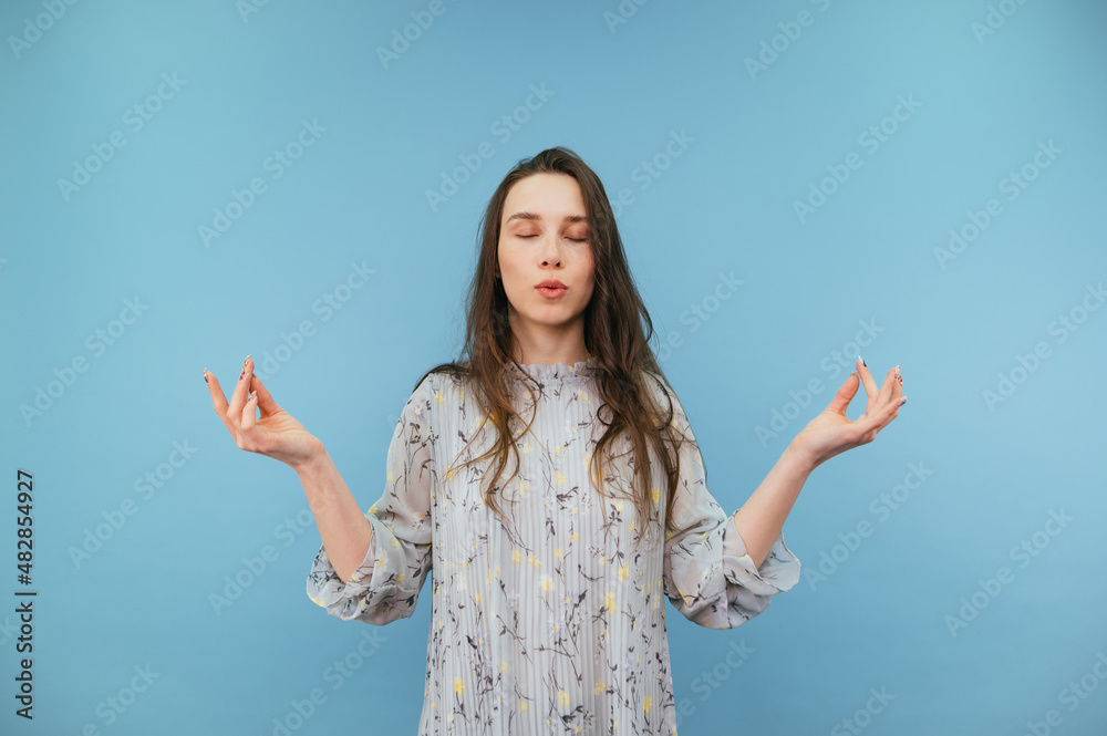 Calm lady in dress meditates with closed eyes on a blue background and breathes calmly. Calm lady in dress meditates with closed eyes on a blue background and breathes calmly.