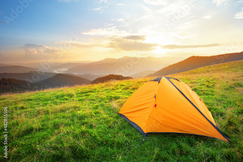 Orange tourist tent in the mountains on a meadow with green grass