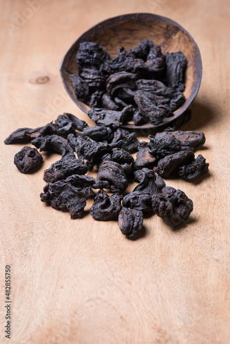 sun dried garcinia fruits scattered on a wooden table top, black shriveled flavoring herb native to south asia, also known as brindle berry, goraka or malabar tamarind, taken in shallow depth of field photo