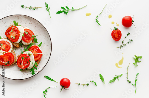 Italian food concept. Open sandwiches with mozzarella, tomatoes and arugula on white plate. Overhead, frame composition © Tania