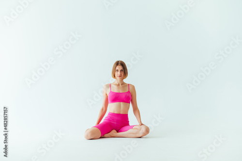 Attractive sports woman in pink sportswear sits on a white background during a workout and looks at the camera.
