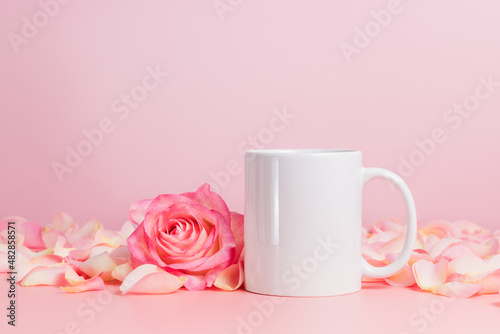 White mockup mug or coffee cup on pink background with rose and petals. Blank mug for template, branding, text or design