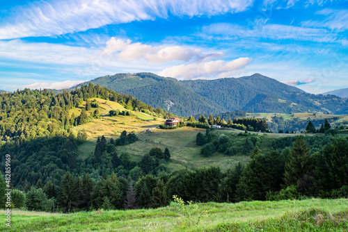 mountain landscape in the Carpathians. Hills with forest in the countryside on a background of mountains with blue sky and white clouds.